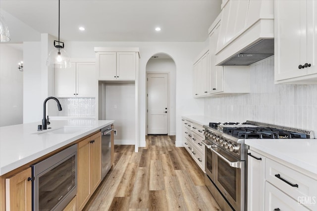 kitchen featuring premium range hood, light wood-type flooring, a sink, arched walkways, and appliances with stainless steel finishes