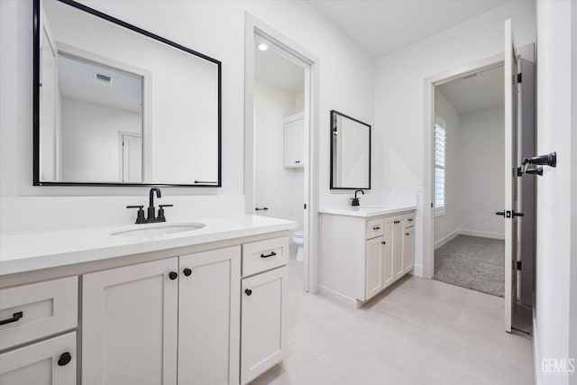 bathroom with two vanities, toilet, visible vents, and a sink