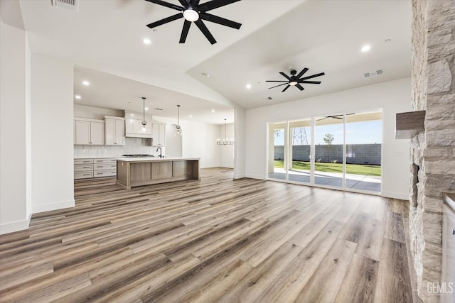 unfurnished living room with light wood-type flooring, visible vents, vaulted ceiling, and ceiling fan with notable chandelier