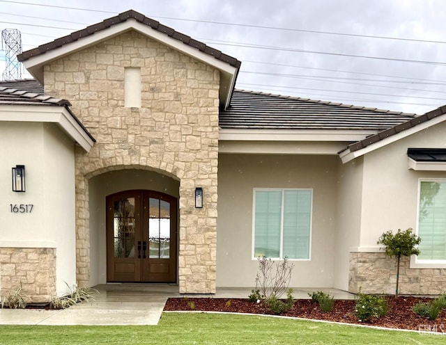 view of exterior entry featuring stucco siding, stone siding, and french doors