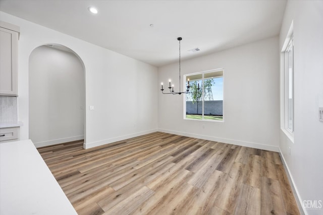 unfurnished dining area featuring visible vents, baseboards, light wood-style flooring, arched walkways, and a notable chandelier