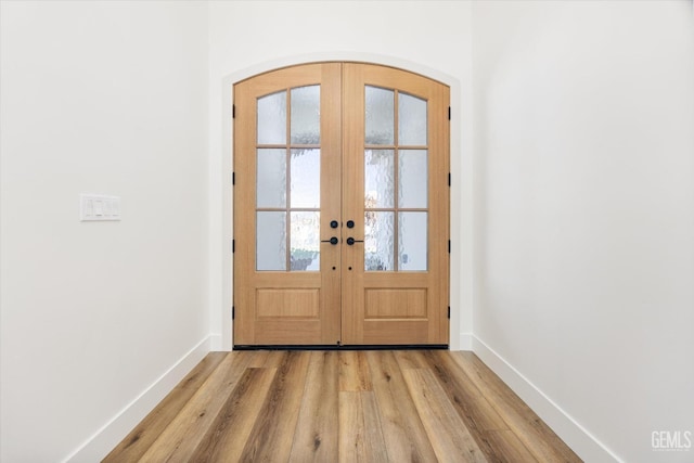 doorway to outside featuring french doors, arched walkways, baseboards, and light wood finished floors