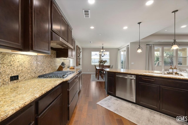 kitchen with sink, stainless steel appliances, light stone countertops, decorative backsplash, and decorative light fixtures