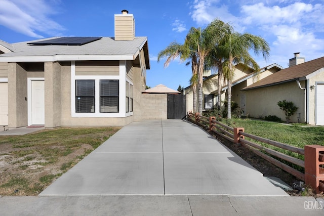 view of home's exterior with a chimney, roof mounted solar panels, fence, and stucco siding