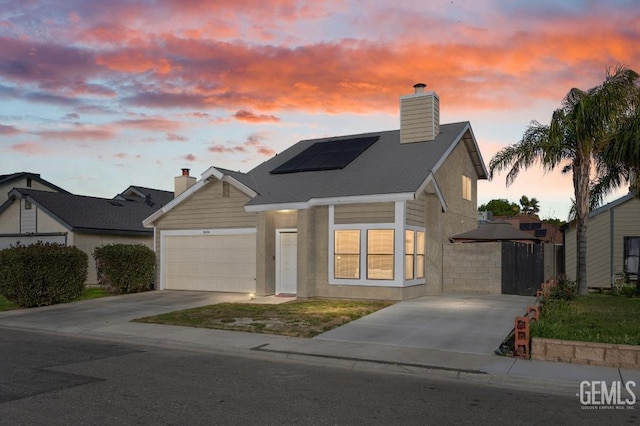 view of front of property featuring a garage, roof mounted solar panels, a chimney, and concrete driveway