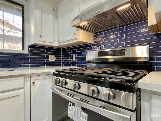 kitchen with stainless steel gas range, exhaust hood, white cabinets, light stone countertops, and backsplash