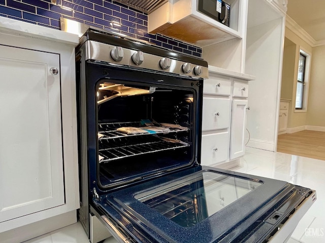 interior details with white cabinetry, tasteful backsplash, ornamental molding, and stove