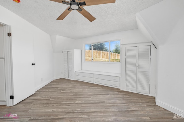 unfurnished bedroom with a textured ceiling, wood finished floors, baseboards, two closets, and a ceiling fan