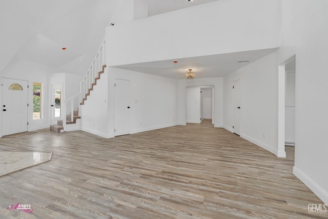 unfurnished living room featuring high vaulted ceiling, light wood-style flooring, stairway, and baseboards