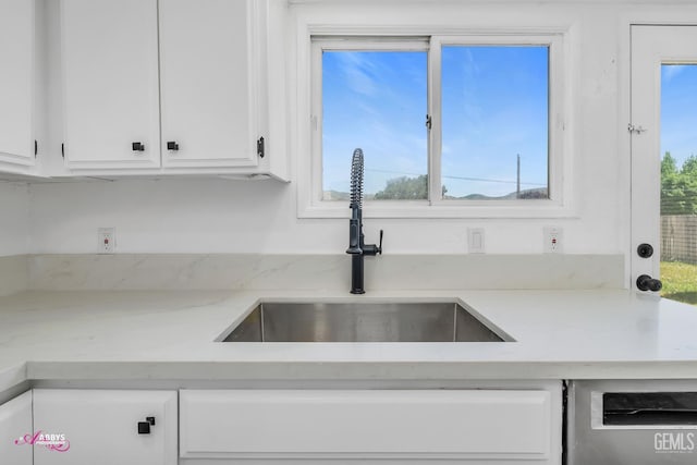 kitchen with a sink, white cabinets, stainless steel dishwasher, and light stone countertops