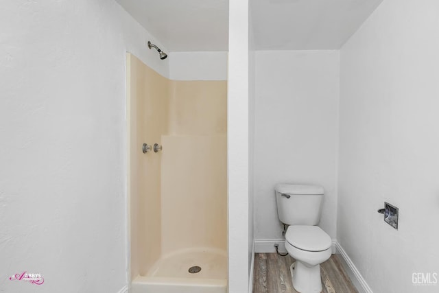 bathroom with wood finished floors, a shower stall, toilet, and baseboards