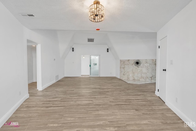 unfurnished living room featuring light wood finished floors, a chandelier, a textured ceiling, and baseboards