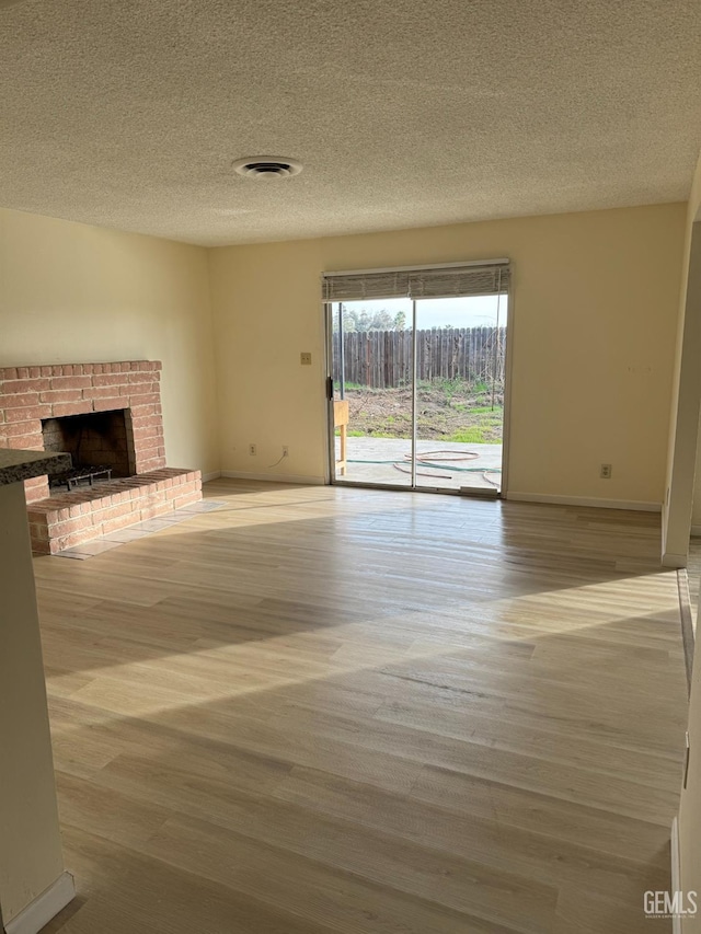 unfurnished living room with a brick fireplace, hardwood / wood-style floors, and a textured ceiling