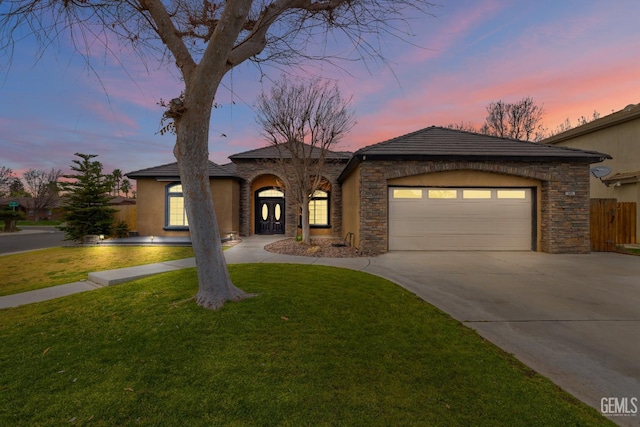 view of front of house with driveway, a lawn, stone siding, an attached garage, and stucco siding