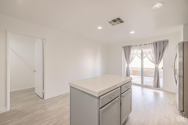 kitchen with stainless steel fridge, light wood-type flooring, tile counters, and gray cabinetry