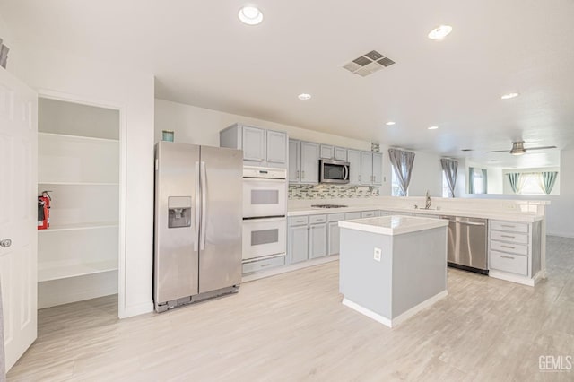 kitchen with ceiling fan, a center island, gray cabinets, decorative backsplash, and appliances with stainless steel finishes