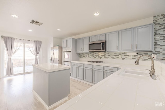 kitchen featuring backsplash, gray cabinetry, stainless steel appliances, sink, and a center island