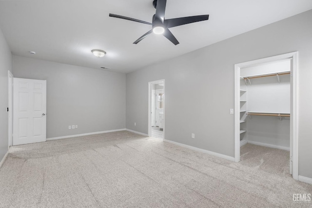 unfurnished bedroom with a walk in closet, a closet, ceiling fan, and light colored carpet