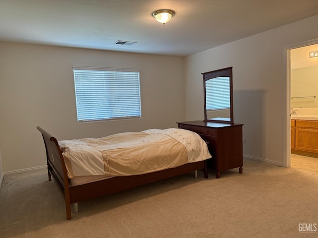 bedroom featuring baseboards, light colored carpet, visible vents, and ensuite bath