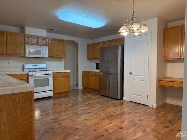 kitchen with an inviting chandelier, tile counters, white appliances, and dark wood-type flooring