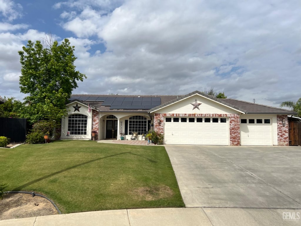 ranch-style house with a front lawn, covered porch, roof mounted solar panels, concrete driveway, and an attached garage