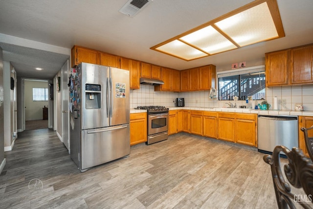 kitchen with sink, light hardwood / wood-style flooring, appliances with stainless steel finishes, tasteful backsplash, and tile counters