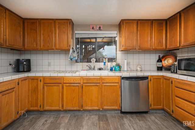 kitchen with dark hardwood / wood-style floors, appliances with stainless steel finishes, tile counters, and decorative backsplash