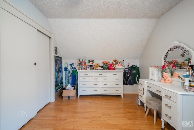 bedroom with vaulted ceiling, light hardwood / wood-style floors, and a textured ceiling