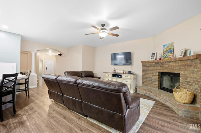 7303 Glenn Miller Ct, Bakersfield, CA 93312 - living room featuring a fireplace, a ceiling fan, decorative columns, arched walkways, and wood finished floors