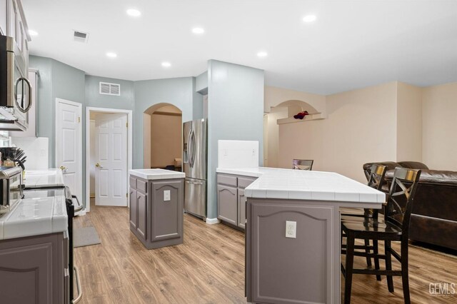 7303 Glenn Miller Ct, Bakersfield, CA 93312 - kitchen with gray cabinets, a peninsula, visible vents, appliances with stainless steel finishes, and arched walkways