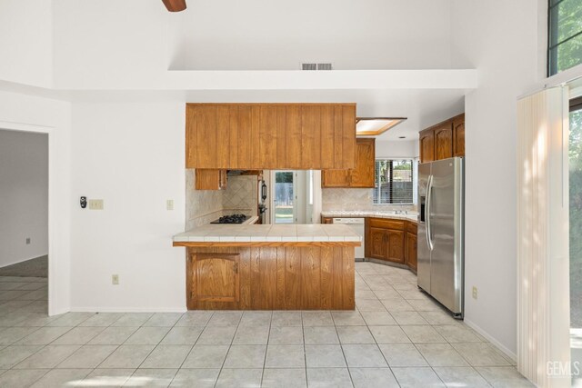 7205 Bandolero Way, Bakersfield, CA 93308 - kitchen with stainless steel fridge, a peninsula, dishwasher, decorative backsplash, and brown cabinets