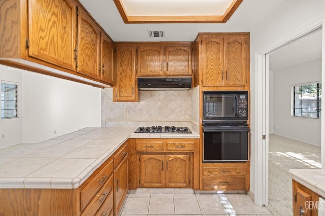 7205 Bandolero Way, Bakersfield, CA 93308 - kitchen with black appliances, under cabinet range hood, brown cabinets, and tasteful backsplash
