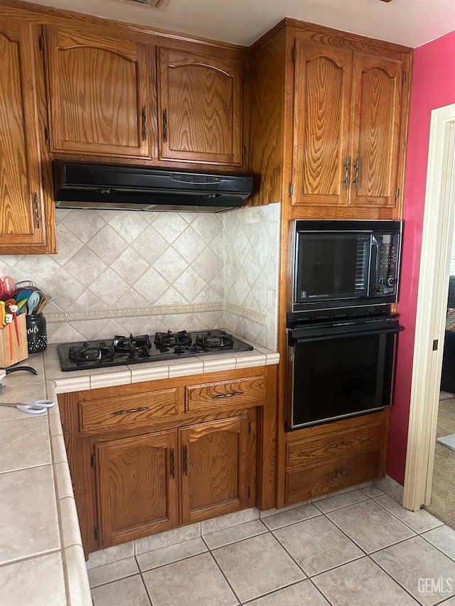 kitchen featuring tile counters, backsplash, light tile patterned floors, and black appliances