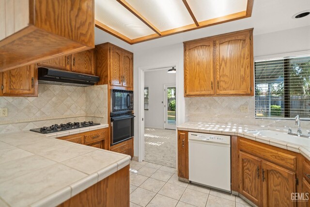 7205 Bandolero Way, Bakersfield, CA 93308 - kitchen with black appliances, under cabinet range hood, light tile patterned floors, tasteful backsplash, and brown cabinets
