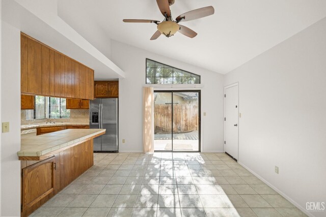7205 Bandolero Way, Bakersfield, CA 93308 - kitchen featuring stainless steel fridge, tile counters, vaulted ceiling, brown cabinetry, and tasteful backsplash