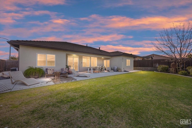 back house at dusk with a yard and a patio