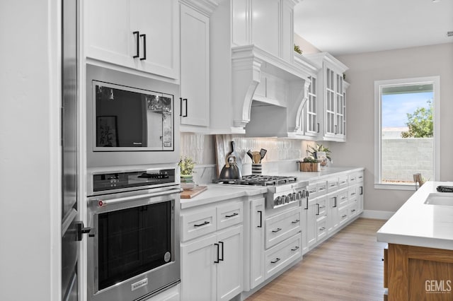 kitchen with stainless steel appliances, light wood-type flooring, white cabinets, and decorative backsplash