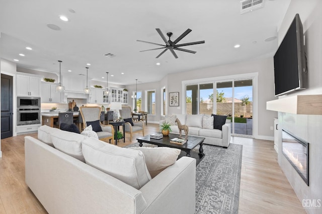 living room featuring a tile fireplace, ceiling fan, and light hardwood / wood-style floors