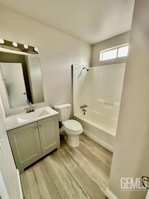 full bathroom with bathtub / shower combination, toilet, a textured ceiling, vanity, and hardwood / wood-style flooring