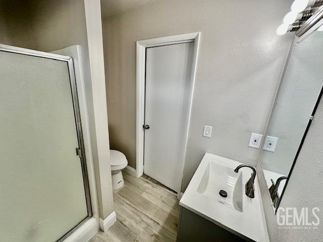 bathroom with walk in shower, vanity, toilet, and wood-type flooring