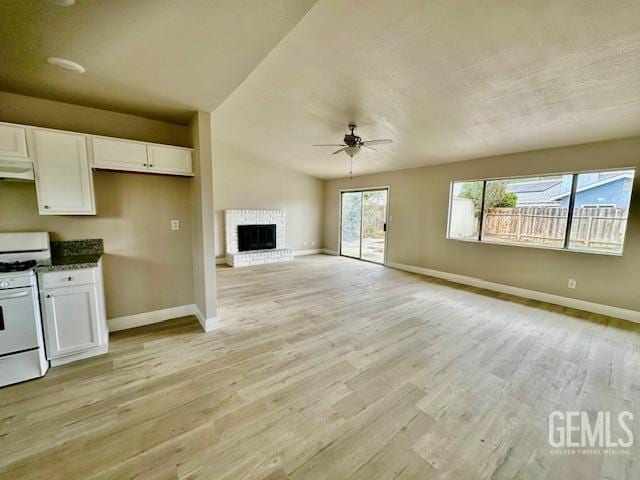 kitchen with white gas stove, a brick fireplace, light wood-type flooring, ceiling fan, and white cabinets