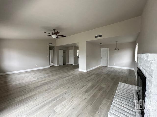 unfurnished living room featuring a stone fireplace, ceiling fan with notable chandelier, and wood-type flooring