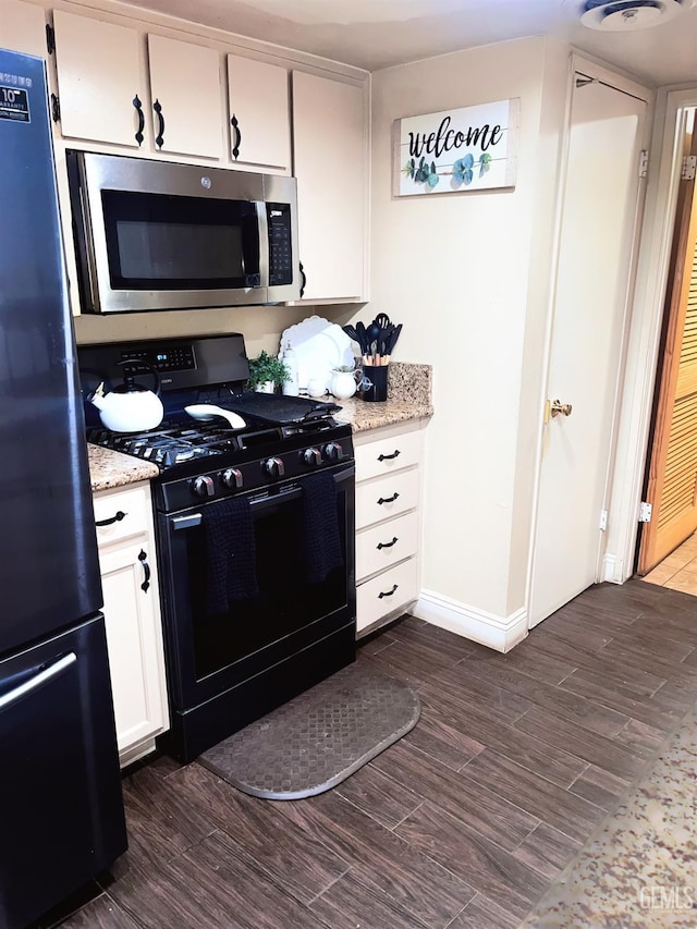 kitchen with black gas range oven, stainless steel microwave, freestanding refrigerator, white cabinets, and dark wood-style flooring