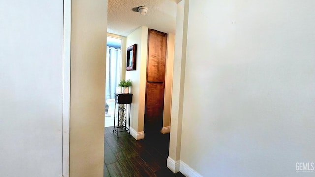 hall featuring dark wood-type flooring, baseboards, and a textured ceiling