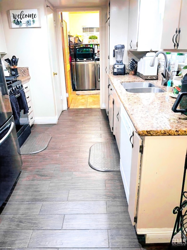 kitchen with light stone counters, black gas range oven, wood finished floors, a sink, and white cabinetry