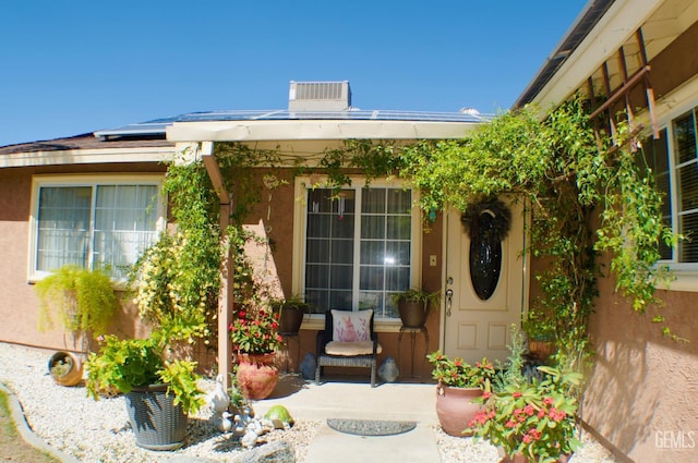 view of exterior entry with stucco siding, solar panels, and central AC