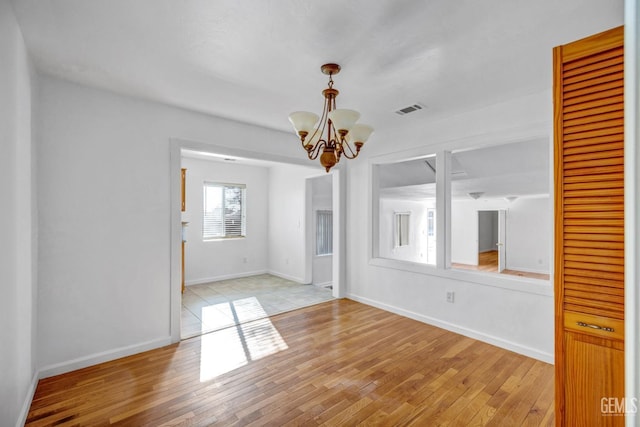 spare room with a notable chandelier and light hardwood / wood-style floors