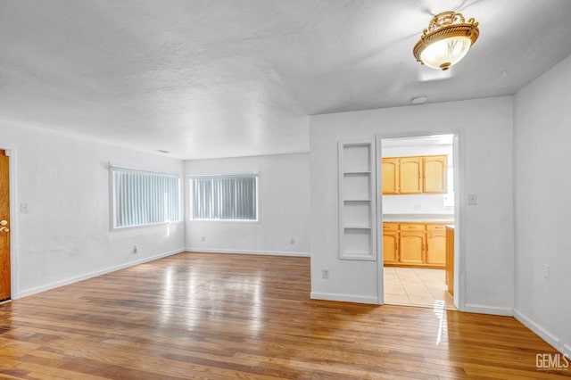 unfurnished living room featuring built in shelves and light hardwood / wood-style floors