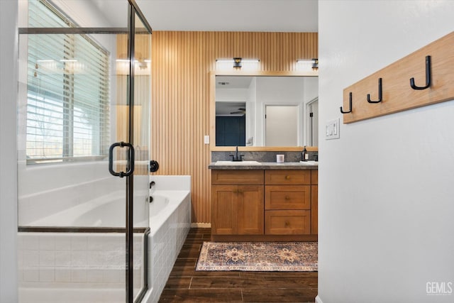 bathroom featuring a bath, double vanity, wood finished floors, a sink, and a stall shower