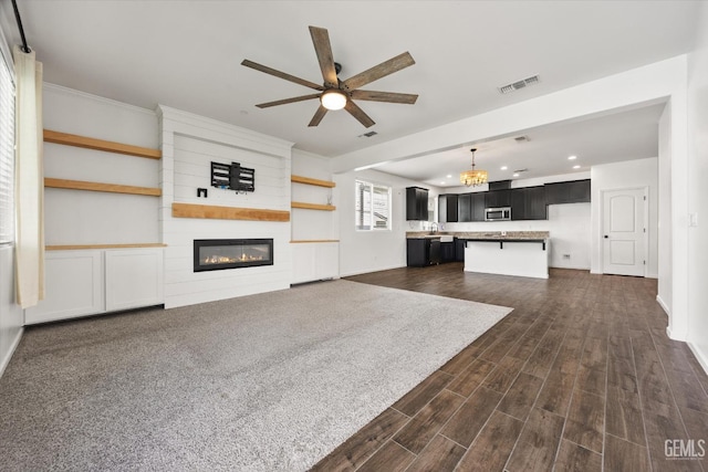 unfurnished living room featuring a fireplace, ceiling fan with notable chandelier, visible vents, recessed lighting, and dark wood-style flooring